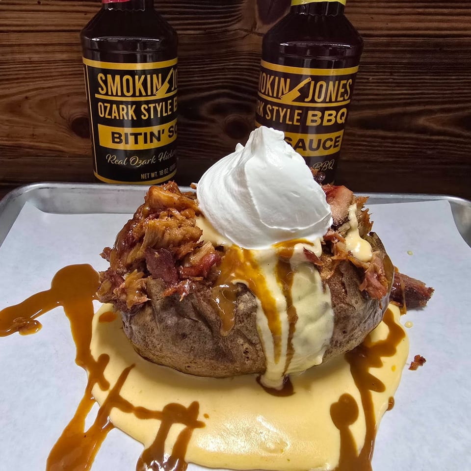 A loaded baked potato with pulled pork, cheese sauce, sour cream, and BBQ sauce.