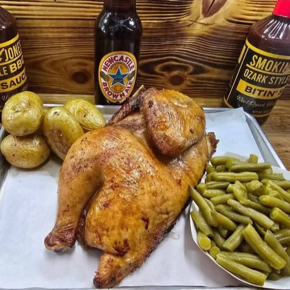 Whole roasted chicken, potatoes, and green beans on a tray with BBQ sauces and Newcastle Brown Ale.